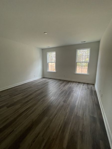 A spacious room with elegant wood flooring, light gray walls, and large windows offering ample natural light.