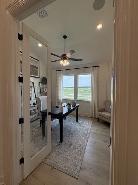 Elegant home office with a glass door, modern fan, soft lighting, and large windows with serene views.