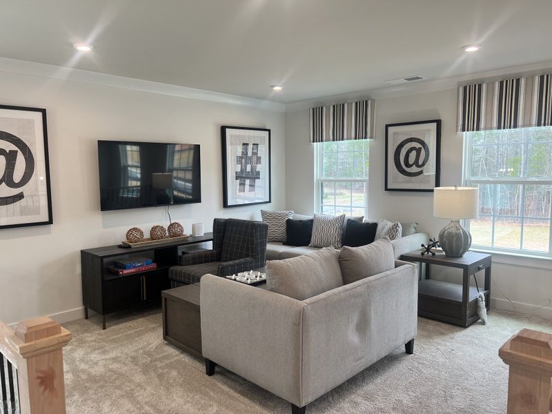 A modern living room featuring a plush sectional, wall art, and a mounted TV with ample natural light.