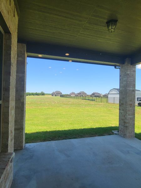 A covered patio with lush green field views, featuring brick pillars and cozy lighting for an inviting outdoor space.