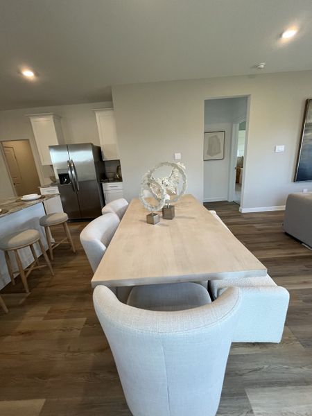A modern dining area featuring a wooden table, plush white chairs, and an open kitchen with sleek stainless appliances.
