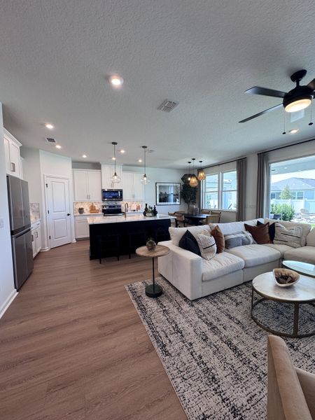 A spacious open-plan living room with elegant decor, wooden floors, a cozy sectional sofa, and modern kitchen fixtures.