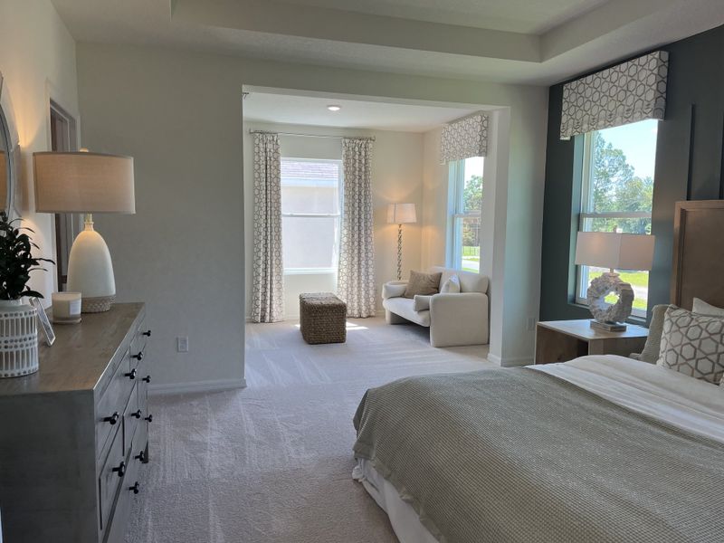 A spacious bedroom with cozy sitting area, elegant lamps, and natural light highlighting soft textures.