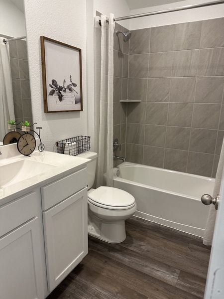 A modern bathroom featuring a sleek white vanity, wood-look flooring, and tasteful gray tile accents.