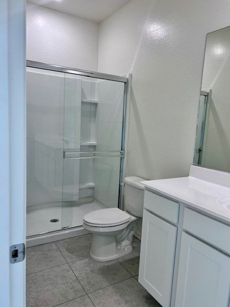 A modern bathroom with a sleek glass shower, white vanity, and neutral tile flooring.