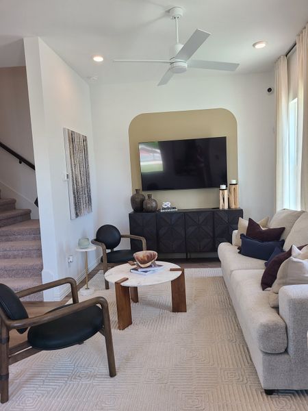 A cozy living room with modern seating, a textured rug, wall-mounted TV, and sleek decor accents.