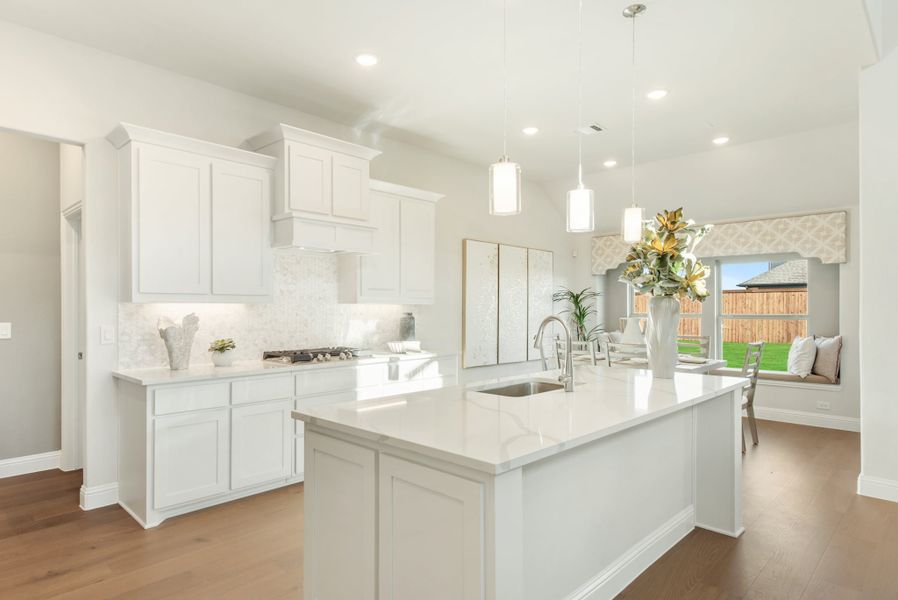 White kitchen with large center island, pendant lights, quartz countertops, and hardwood floors