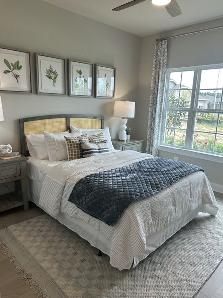 A cozy bedroom with botanical art, a plush bed, elegant nightstands, and a large window for natural light.