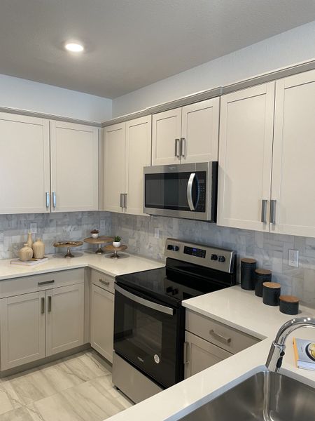 A sleek kitchen featuring modern cabinetry, stainless steel appliances, and marble backsplash with bright lighting.