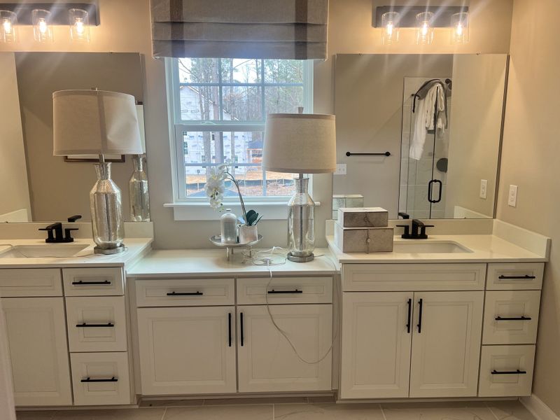 A spacious bathroom with dual sinks, elegant lighting, black fixtures, and a large window.