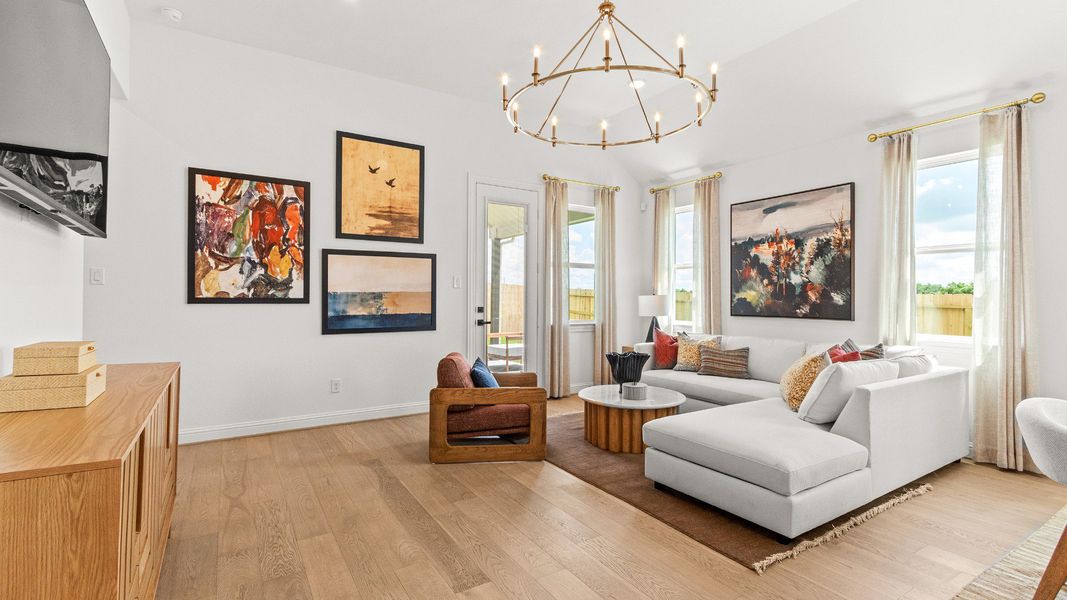 Bright living room featuring a modern gold chandelier and natural light from expansive windows in Azalea community home.