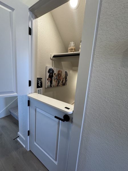 A cozy under-stairs nook with a half-door, pet-themed decor, and jar storage, perfect for a pet-friendly home.