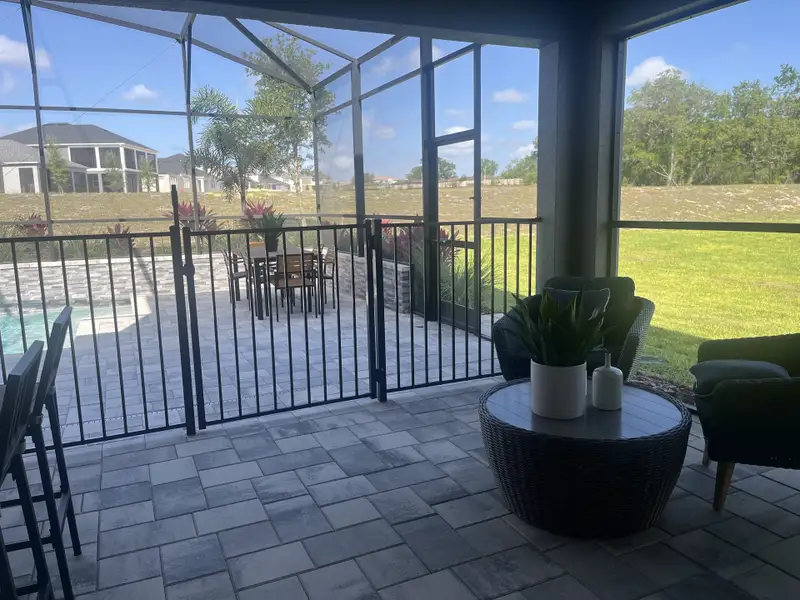 A cozy screened-in patio with outdoor seating, potted plants, and paving stones, overlooking a pool and green lawn. A cozy screened-in patio with outdoor seating, potted plants, and paving stones, overlooking a pool and green lawn.