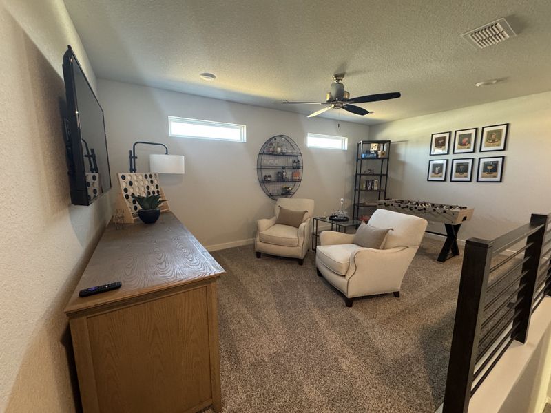 A cozy game room with plush seating, wall art, a foosball table, TV, and modern decor on soft carpet flooring. A cozy game room with plush seating, wall art, a foosball table, TV, and modern decor on soft carpet flooring.