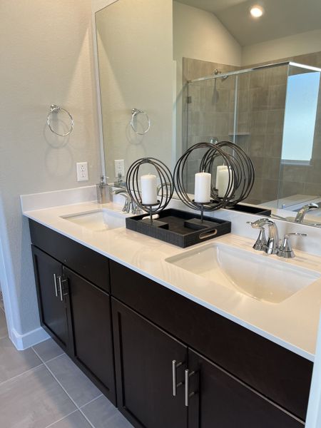 A sleek bathroom featuring a dual-sink vanity with dark cabinetry, elegant fixtures, and modern decorative accents.