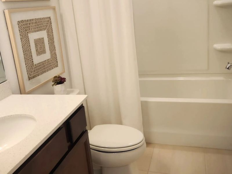 A chic bathroom with a sleek white vanity, modern artwork, and a pristine bathtub.