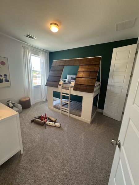 A cozy kids' bedroom with a unique cabin-themed bed, green accent wall, and soft carpet flooring. Stylish and fun space.