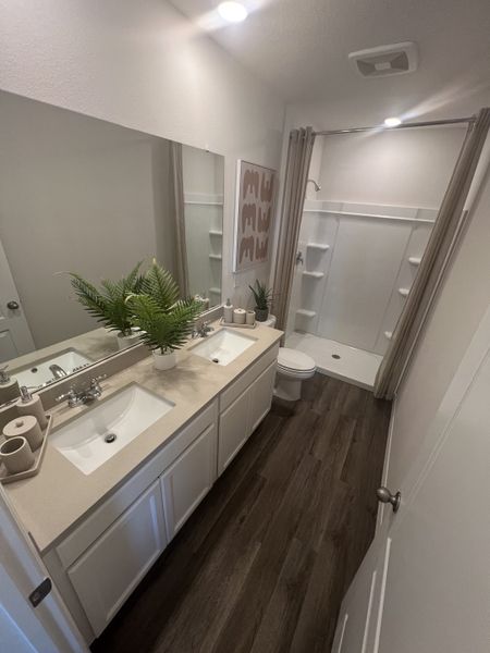 A modern bathroom featuring dual sinks, elegant dark wood flooring, and a spacious shower area.