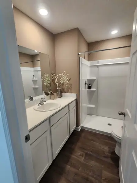 A cozy bathroom with wood flooring, beige walls, white cabinetry, and a spacious walk-in shower.