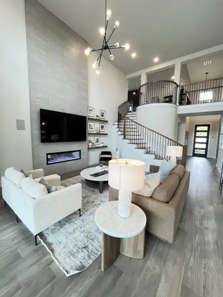 A contemporary living room with a fireplace, modern chandelier, elegant staircase, and cozy seating arrangement. A contemporary living room with a fireplace, modern chandelier, elegant staircase, and cozy seating arrangement.
