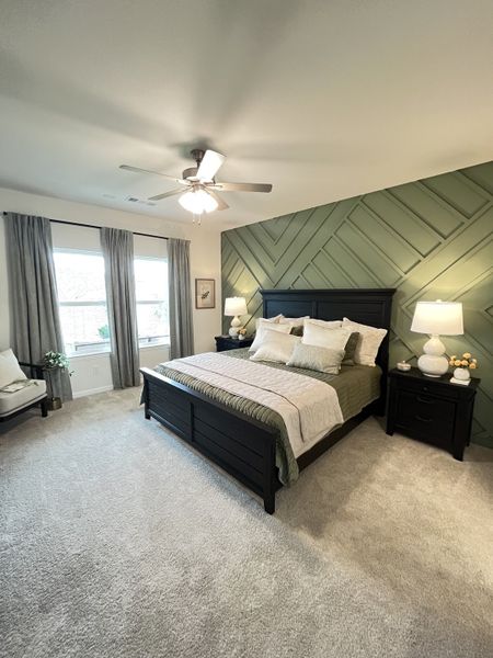 A serene bedroom with textured green accent wall, cozy beige carpet, and elegant dark wood furniture.