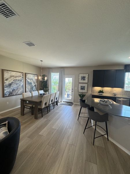 Modern dining area with elegant wood flooring, a chic table setting, and stylish dark cabinetry in the kitchen. Modern dining area with elegant wood flooring, a chic table setting, and stylish dark cabinetry in the kitchen.