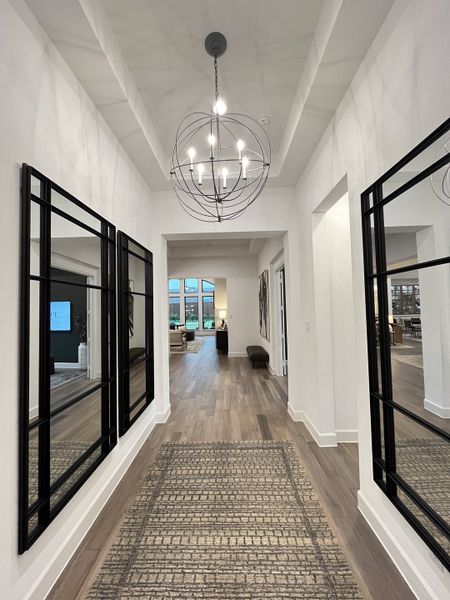 A bright hallway with modern lighting, mirrored walls, and a patterned rug leading to an open living area.