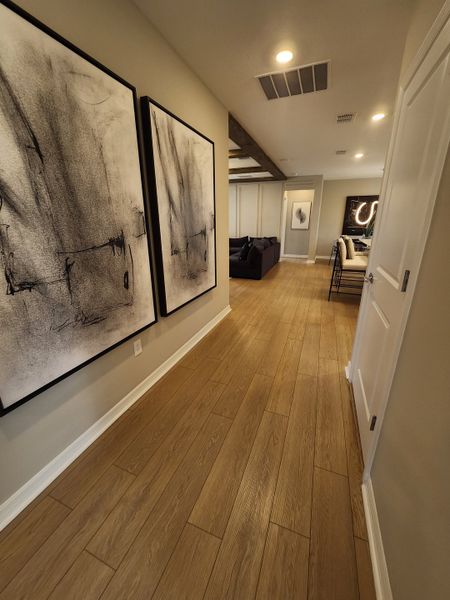 A modern hallway with wooden floors, abstract artwork, and recessed lighting leading to a cozy living area. A modern hallway with wooden floors, abstract artwork, and recessed lighting leading to a cozy living area.