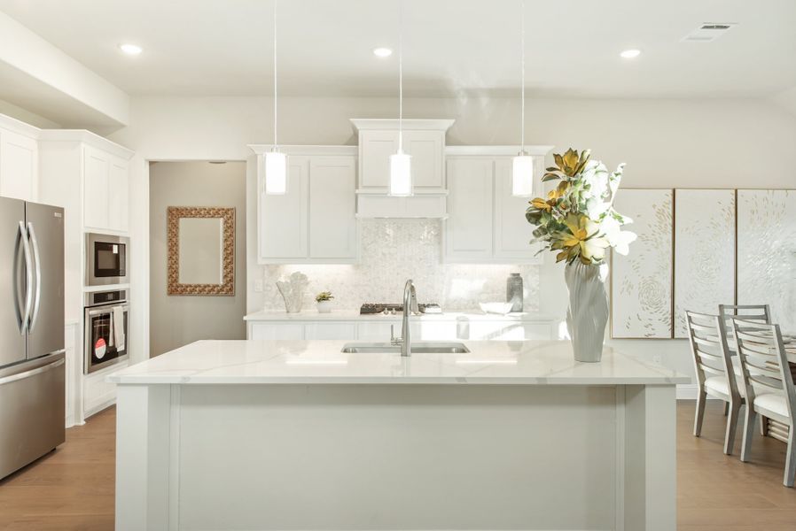 White kitchen with large island, quartz countertops, pendant lights, and stainless steel appliances