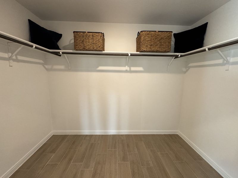 A spacious walk-in closet featuring sleek shelves, wicker baskets, and elegant wood flooring.