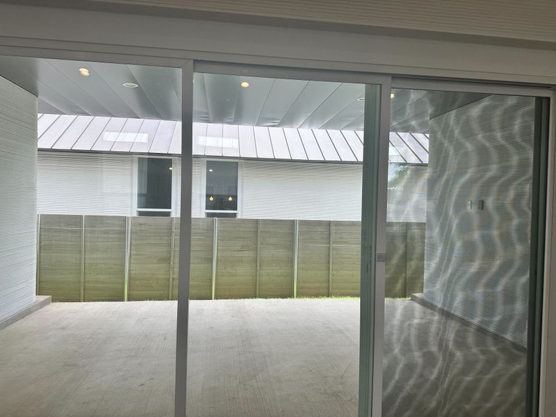 A bright patio with sliding glass doors, wood panel fence, and modern ceiling, creating a tranquil outdoor space.