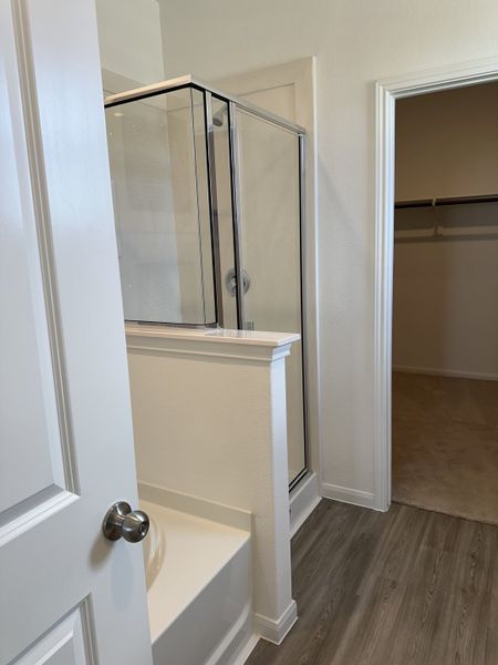 A modern bathroom with a sleek glass shower, white tub, and elegant grey vinyl flooring.