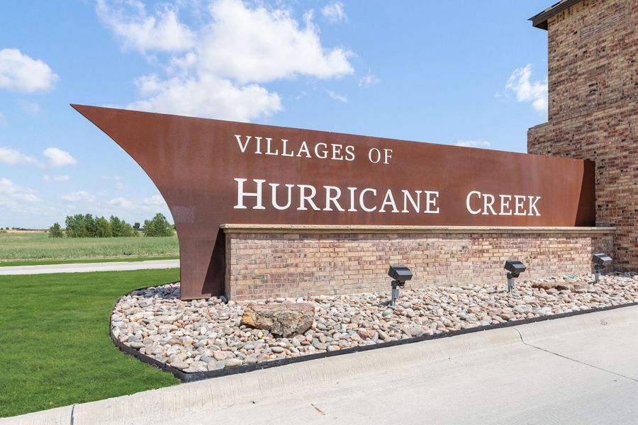 Villages of Hurricane Creek neighborhood entrance sign with metal and brick monument, rock landscaping, and green lawn