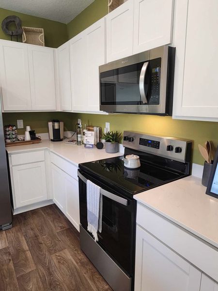 A contemporary kitchen featuring sleek white cabinets, stainless steel appliances, and warm wood flooring.