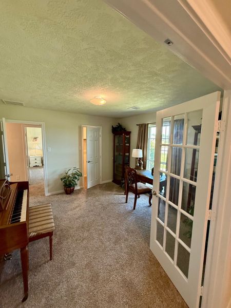 A cozy room with French doors, a piano, carpeted floors, and a window-side desk. Perfect for music and study.