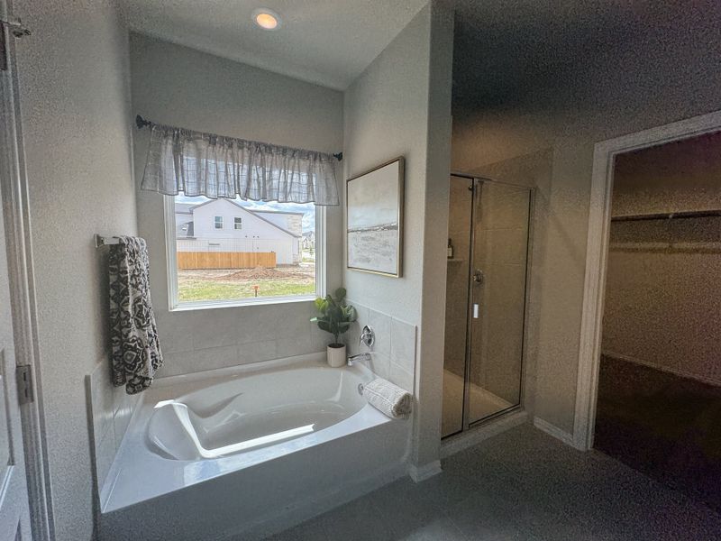 A cozy bathroom featuring a tiled bathtub, glass shower, and natural light streaming through the window.