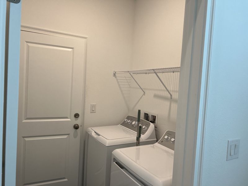 A compact laundry room with white appliances, wire shelving, and a simple design for efficient functionality.