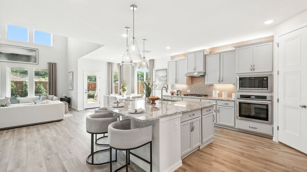 Opulent granite island, pristine gray cabinetry, and chic pendant lights in Green Oaks Preserve kitchen. Opulent granite island, pristine gray cabinetry, and chic pendant lights in Green Oaks Preserve kitchen.