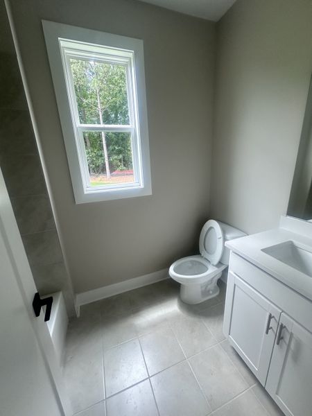 A bright bathroom featuring a single window, white vanity, and modern fixtures with neutral tile flooring. A bright bathroom featuring a single window, white vanity, and modern fixtures with neutral tile flooring.