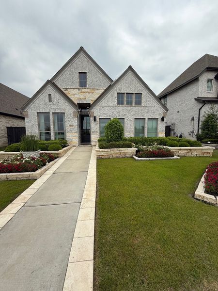 A charming light brick home with peaked roofs and manicured landscaping in Harvest Green 45' by Perry Homes (Richmond, TX).