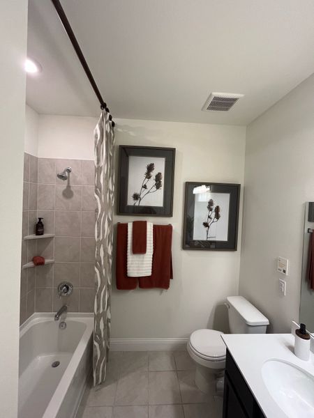 A modern bathroom featuring a tiled bathtub, elegant fixtures, and tasteful wall art.