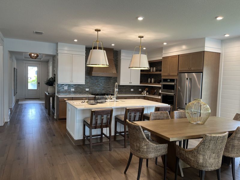 A modern kitchen with sleek cabinetry, stainless steel appliances, and a cozy dining area featuring woven chairs and elegant lighting.