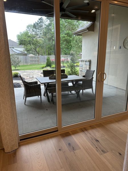 A cozy patio view with woven furniture, stone accents, and lush greenery seen through glass doors.