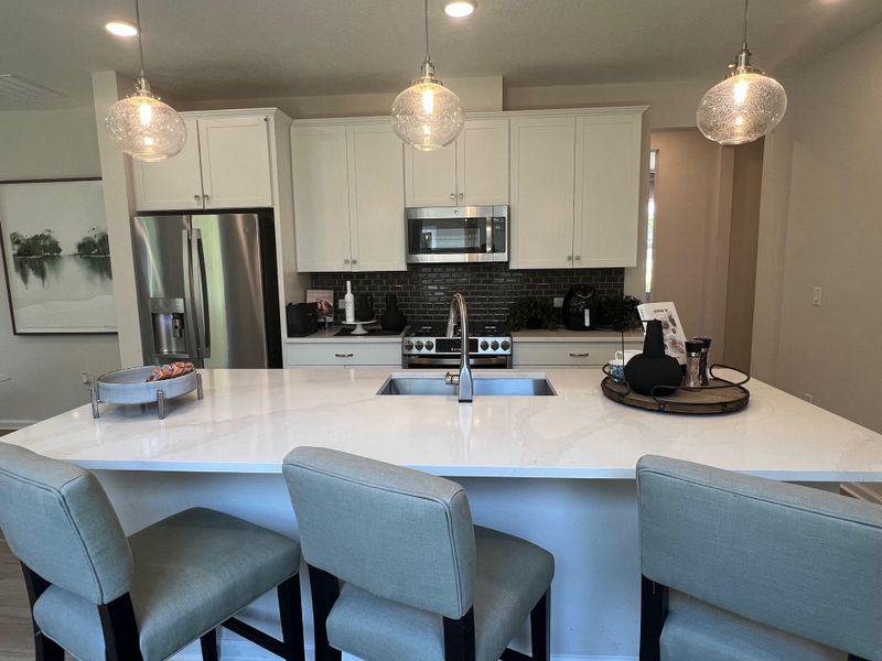 A modern kitchen with white cabinets, stainless-steel appliances, and a sleek island with pendant lighting.