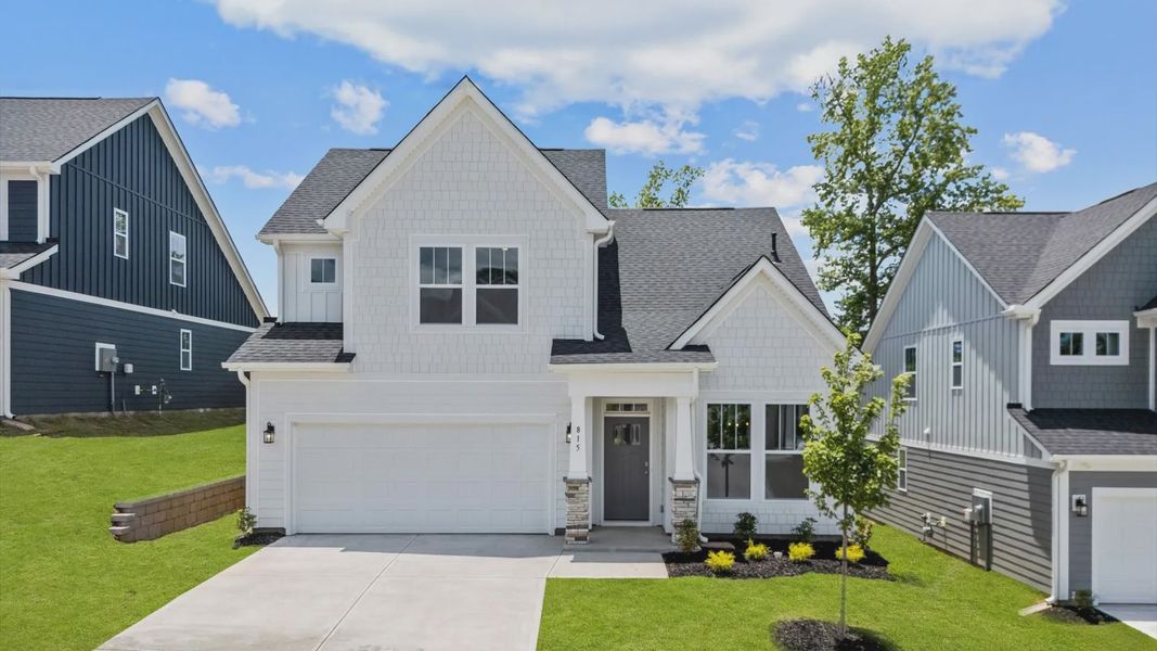 Bright white exterior home with gray door and stone details at Pleasant Falls by DRB Homes in Moore, SC