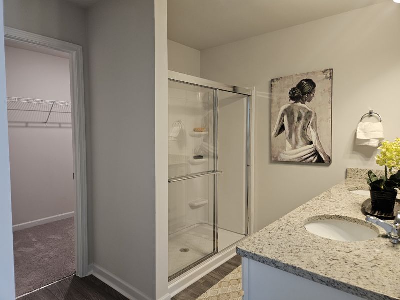 A modern bathroom featuring a granite double vanity, glass shower, and elegant artwork.