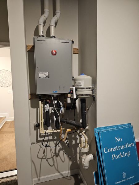 A neat utility area featuring a tankless water heater and pipes, alongside construction signs in a modern interior space.