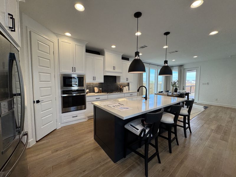 A modern kitchen with sleek white cabinetry, a large island, black pendant lighting, and wooden flooring.