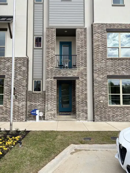 A modern brick facade with a blue door and balcony in Collin Creek by Mattamy Homes (Plano, TX).