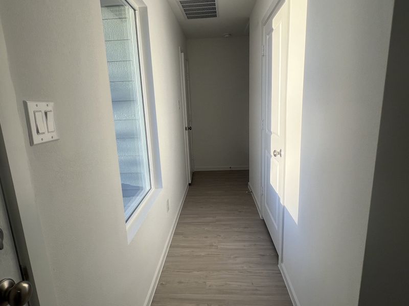 A bright hallway with light wood flooring, white walls, and a large window for natural light.